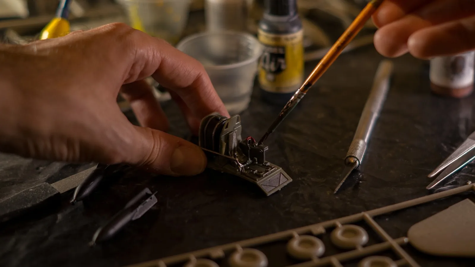 Hobbyist detailing a small scale model with a fine brush at a workbench