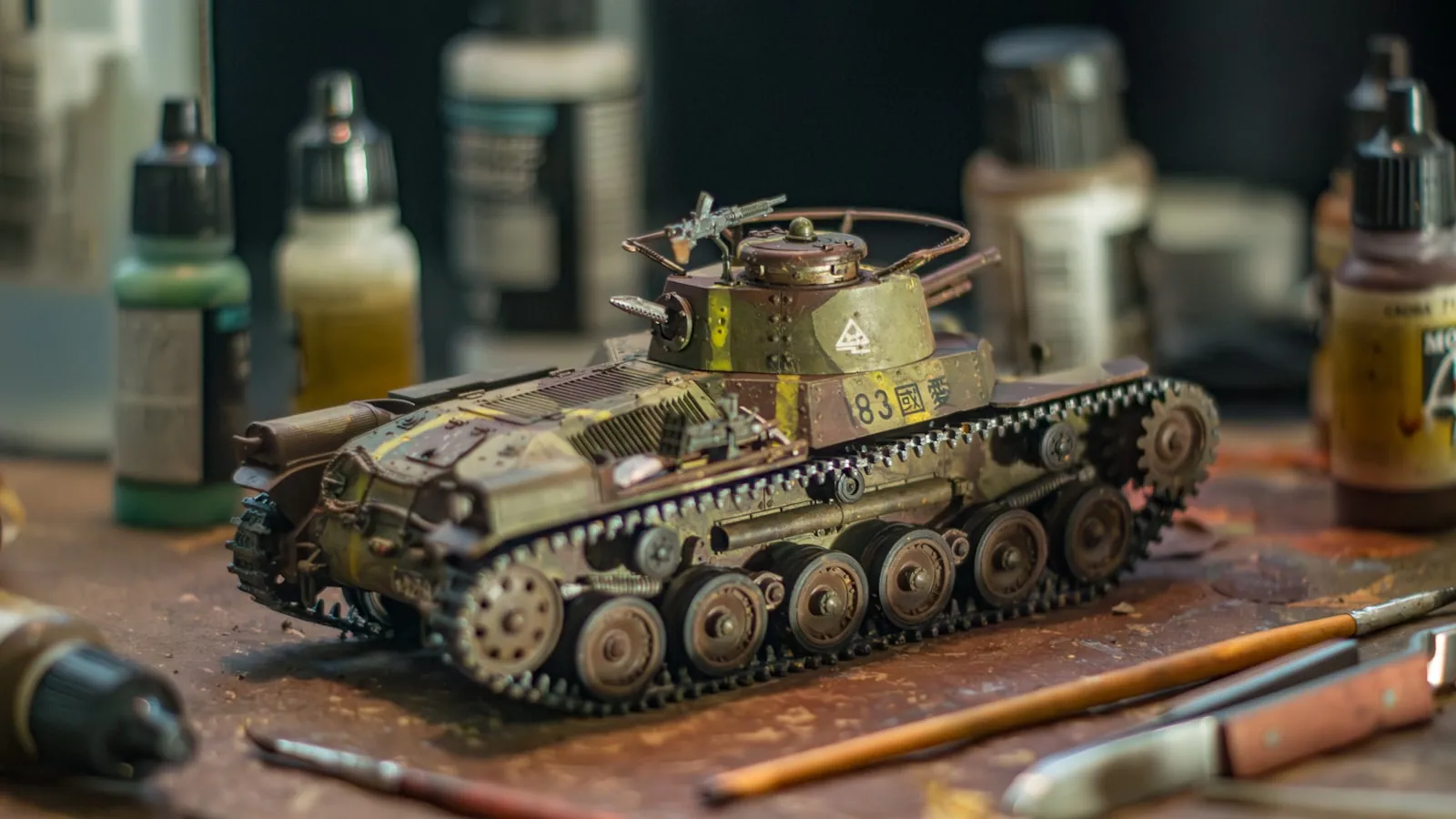 Painted model tank on a hobby desk surrounded by paints and brushes